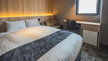 A hotel room with a bed, a desk, a chair, and a window.