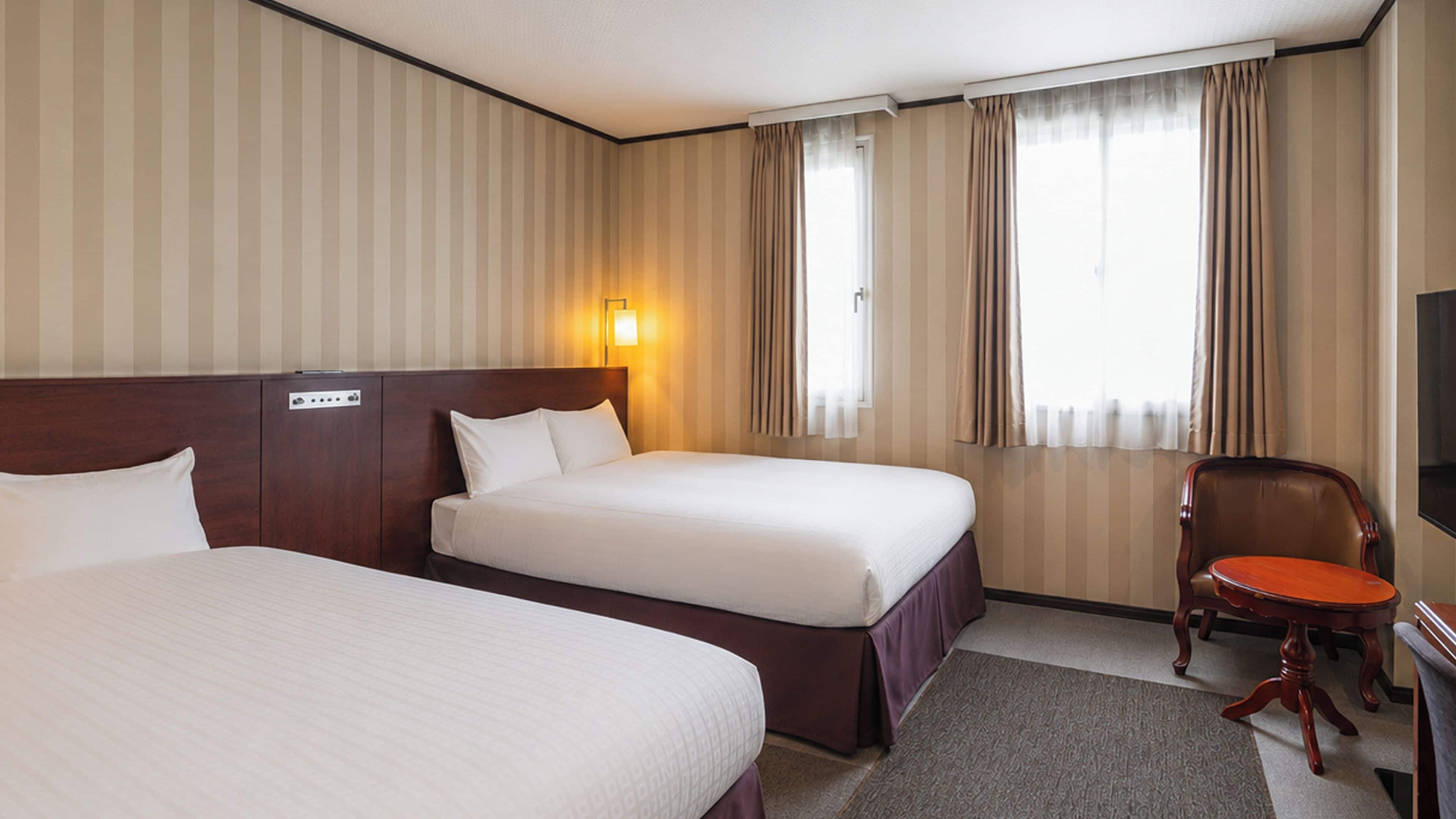 A hotel room with two beds, a desk, a chair, a TV, and a window with curtains.