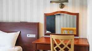 Habitación de hotel con cabecera de madera, mesita de noche, una silla, un espejo y una lámpara de pared.