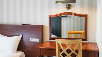 Habitación de hotel con cabecera de madera, mesita de noche, una silla, un espejo y una lámpara de pared.