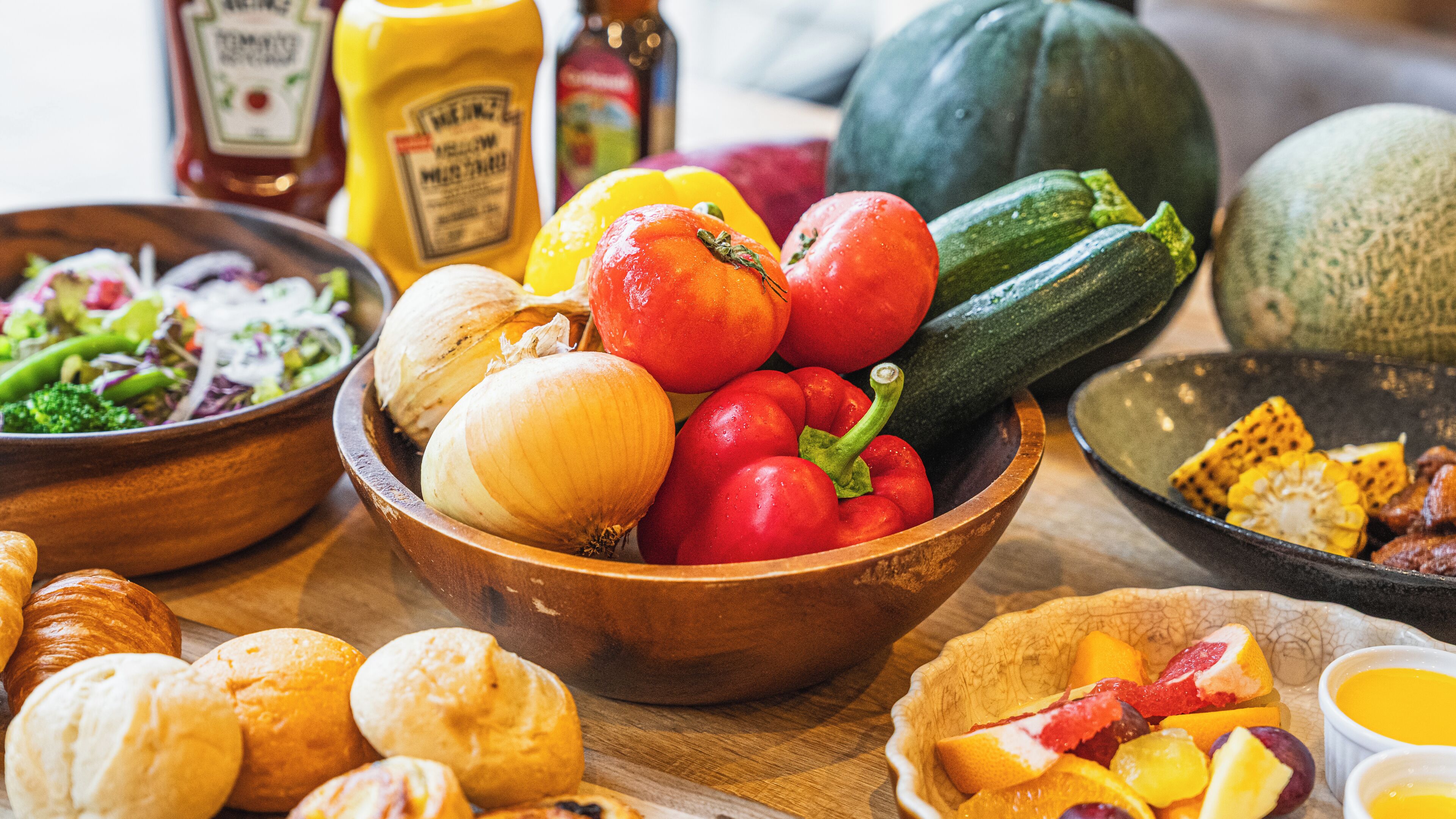 A wooden bowl filled with vegetables, a plate of bread, and a bowl of fruit.