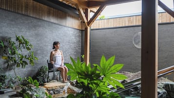 A person seated on a chair in a covered outdoor area with a stone wall and wooden beams.