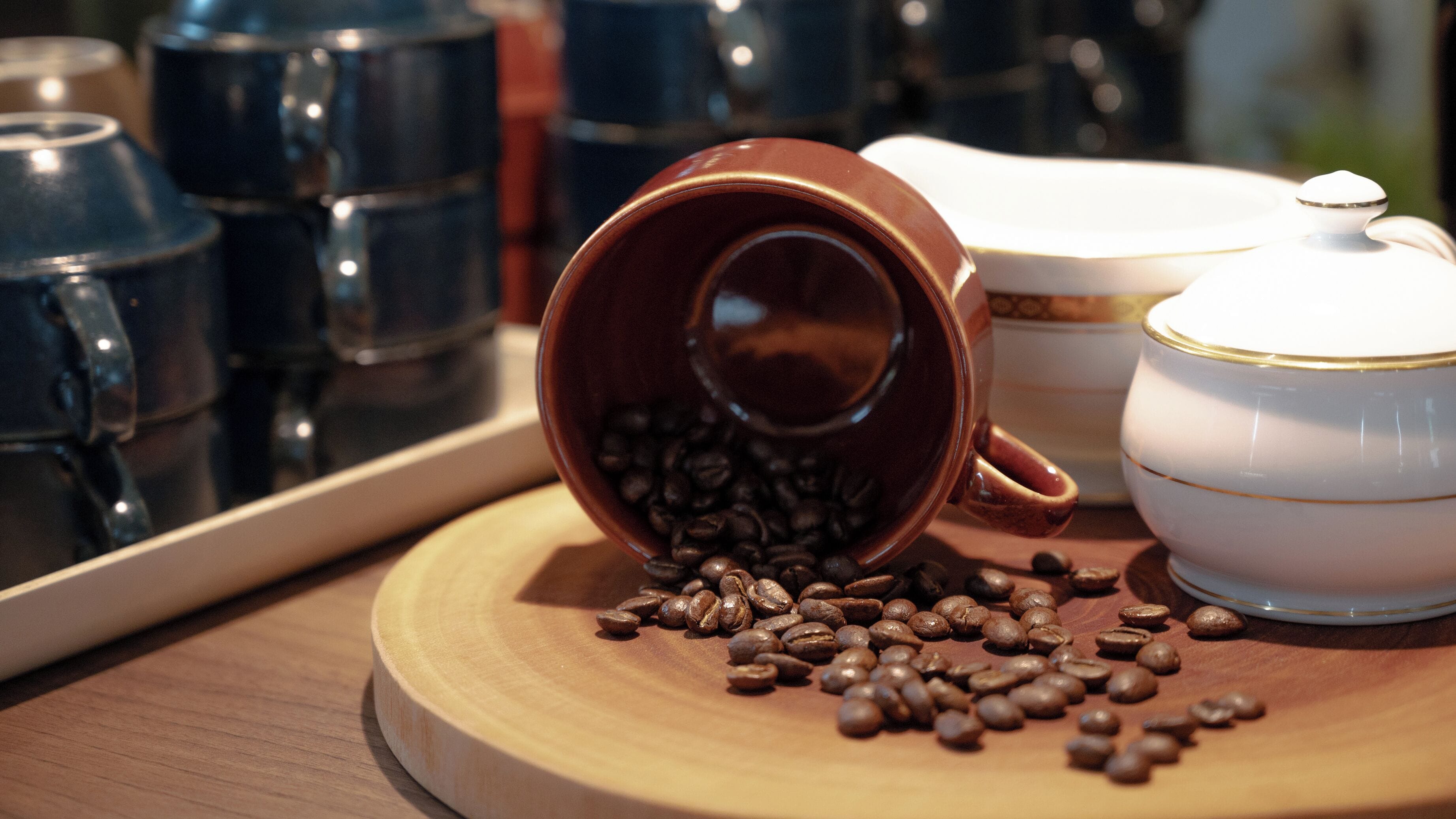 Une tasse à café s’est renversée, et des grains de café se sont répandus sur un plateau en bois.