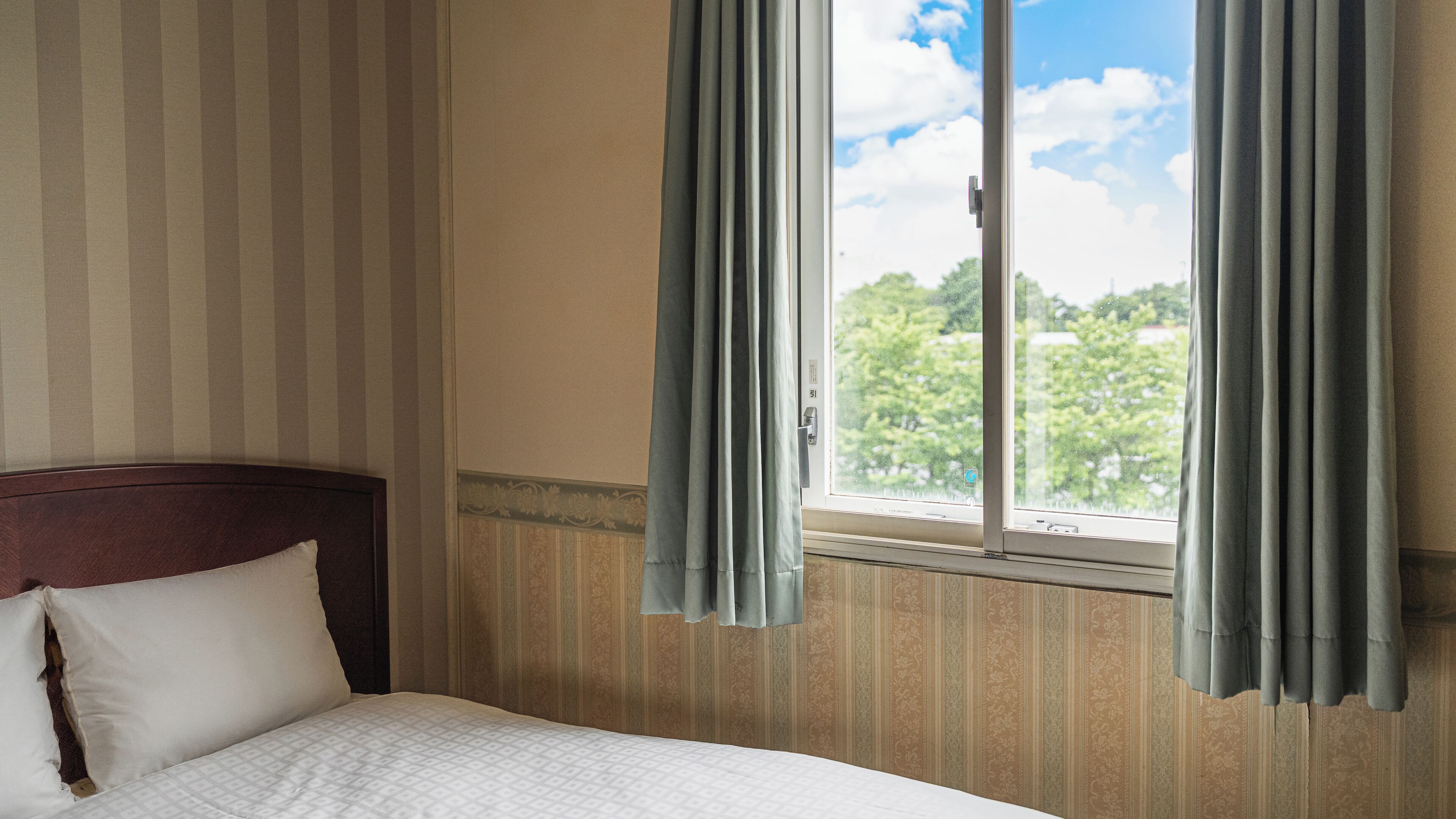 A hotel room with a bed, curtains, a window, and a view of greenery.
