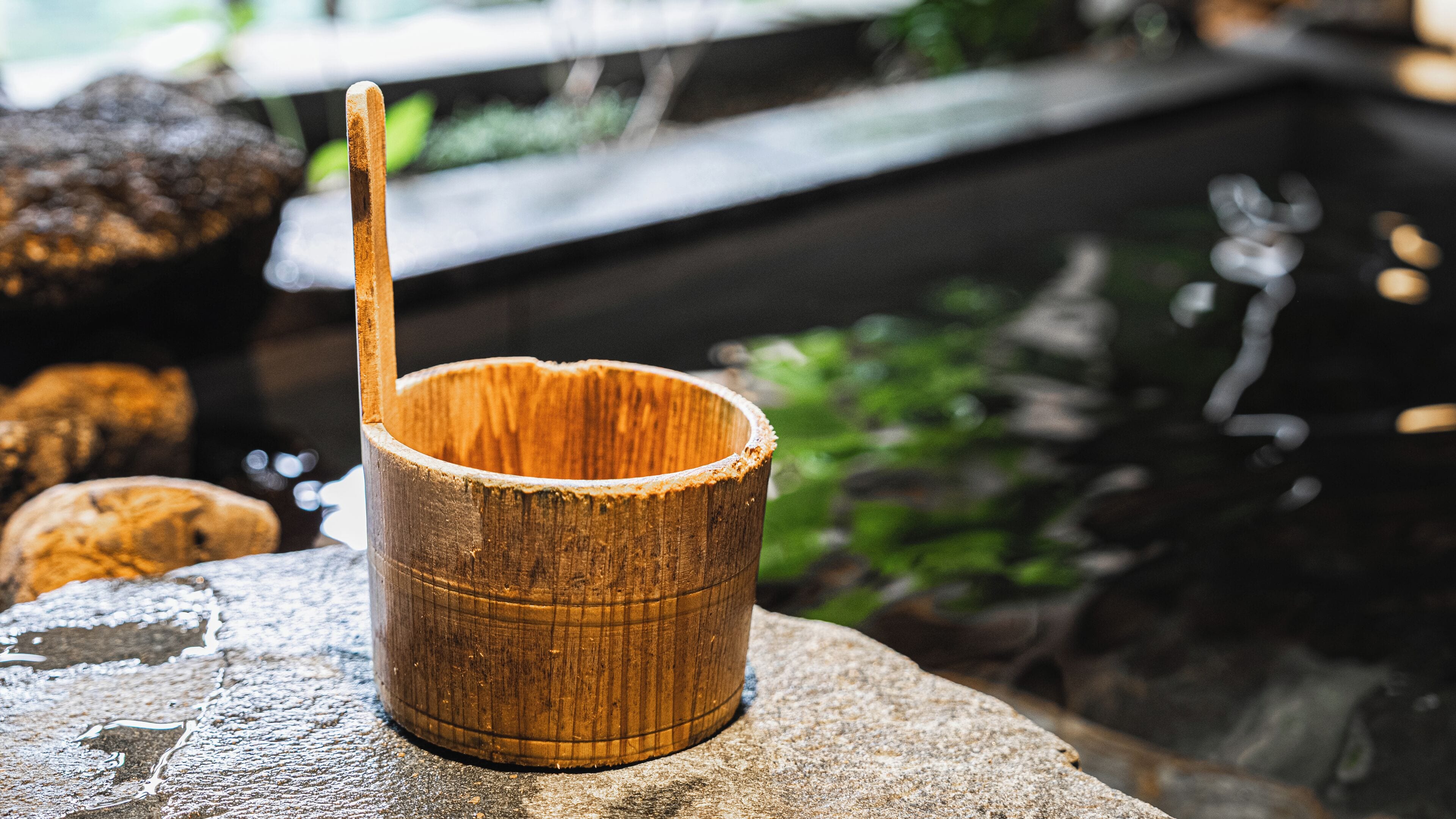 A wooden cup with a spoon on a stone surface near a body of water.