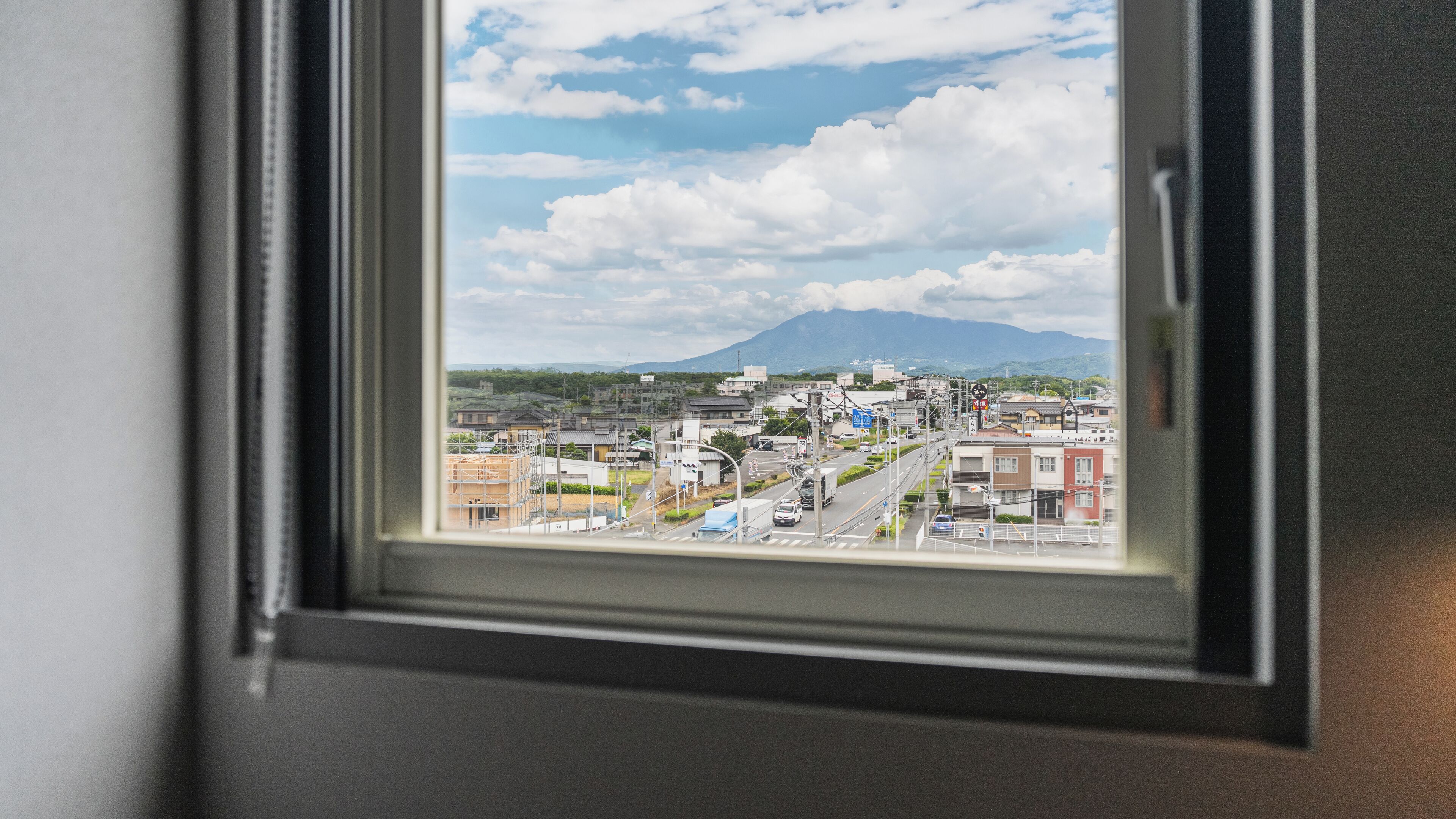 A window view of a cityscape with buildings, roads, and a mountain in the background.