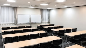 Un salón de conferencias con varias mesas y sillas, pizarras blancas y cortinas.