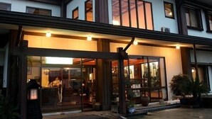 A two-story building with a glass storefront and a visible interior with seating. - Tsukuba Town Hotel (Joso)