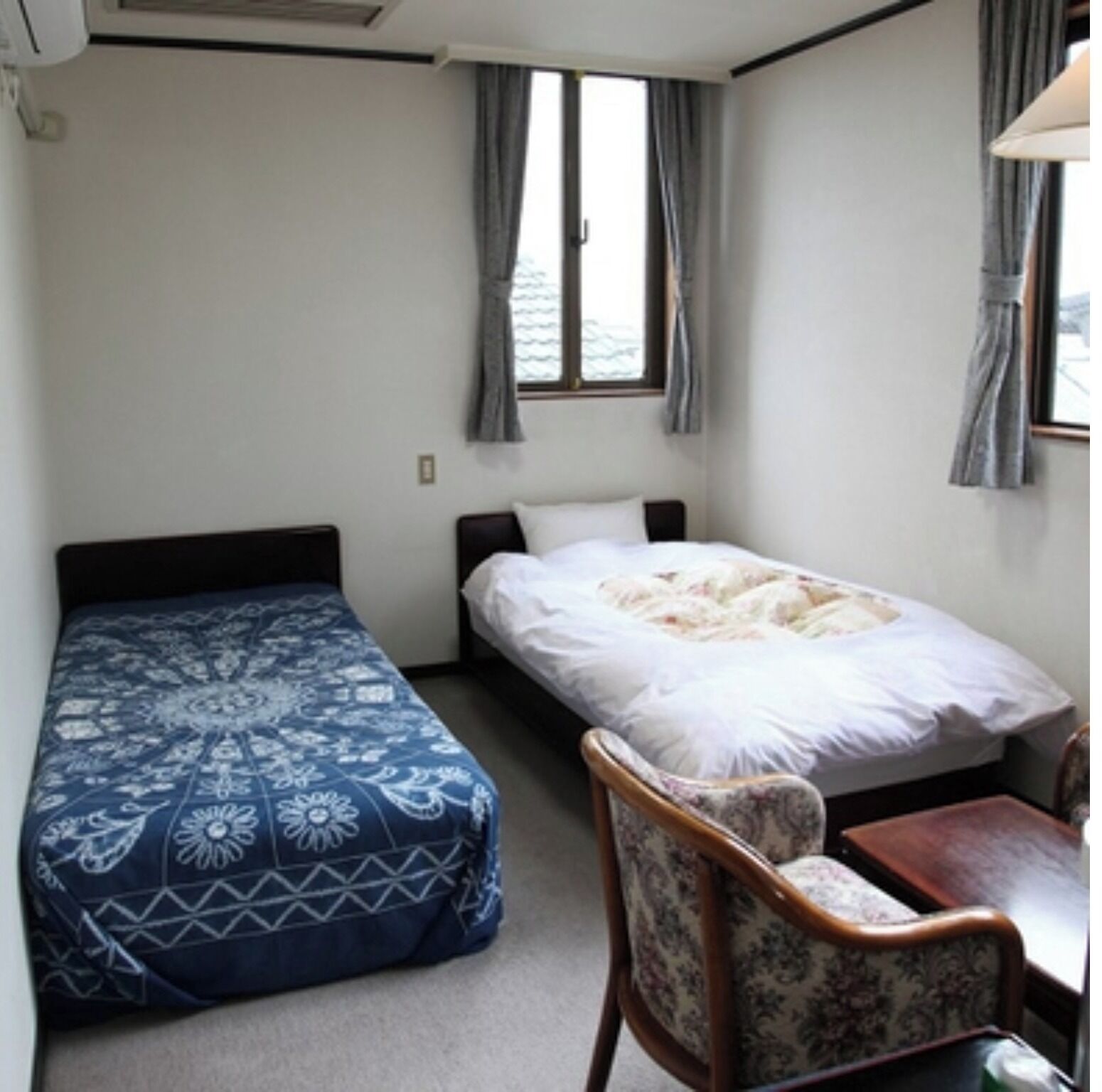Een kleine, eenvoudige kamer met twee bedden, een stoel en een tafel.