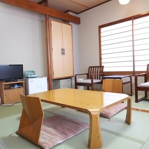 A traditional Japanese room with tatami flooring, a low wooden table, and a television on a cabinet. - Hotel Harumoto (Nikko)