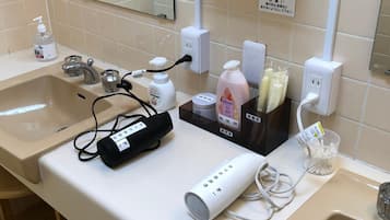 A bathroom with a sink, mirror, and various toiletries including a hairdryer, bottle of lotion, and toothbrushes.