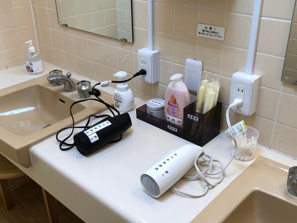 A bathroom with a sink, mirror, and various toiletries including a hairdryer, bottle of lotion, and toothbrushes. - Hotel Harumoto (Nikko)