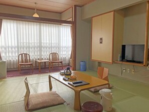 Una habitación tradicional japonesa con suelo de tatami, una mesa baja con cojines, un televisor y un armario.