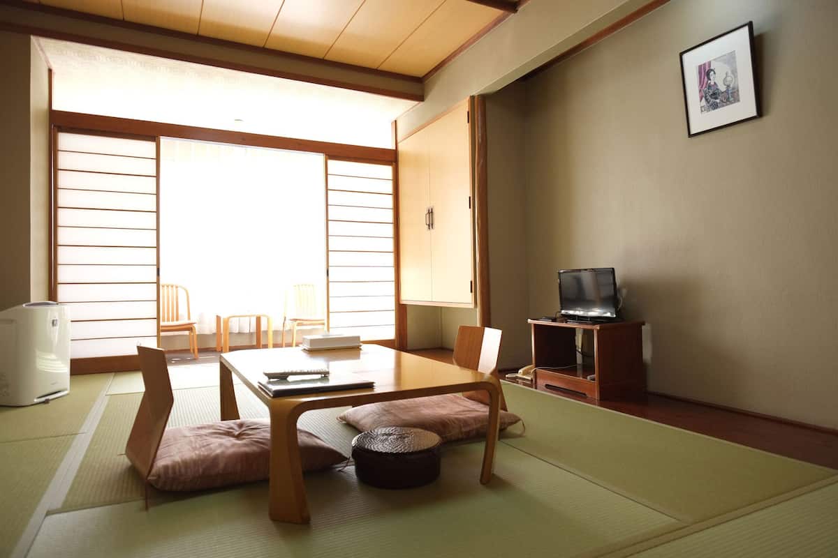 A traditional Japanese room with tatami flooring, a low table, chairs, a television, and a sliding door.