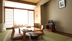 Una habitación tradicional japonesa con suelo de tatami, una mesa baja, cojines, televisión y puertas correderas.
