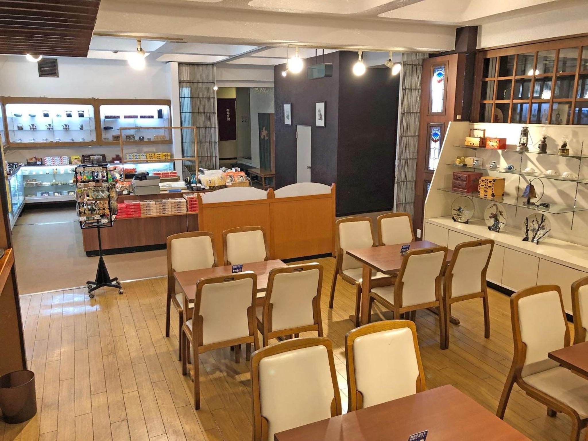 A cafe with wooden tables and chairs, a display counter with various items, and a wall with decorative items.