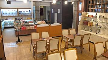 A cafe with wooden tables and chairs, a display counter with various items, and a wall with decorative items.