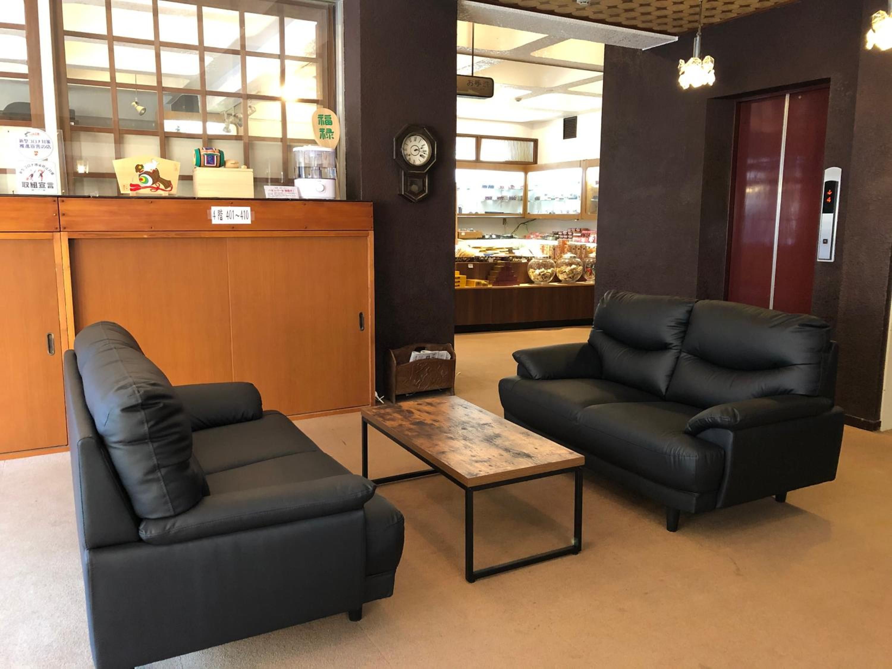 A lobby with two black leather sofas, a wooden coffee table, a reception desk, and a clock on the wall.