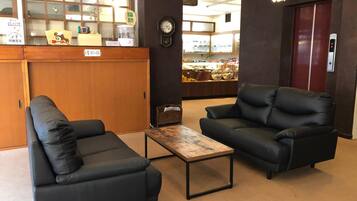 A lobby with two black leather sofas, a wooden coffee table, a reception desk, and a clock on the wall.