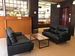Un vestíbulo con dos sofás de cuero negro, una mesa de centro de madera, un mostrador de recepción y un reloj en la pared.