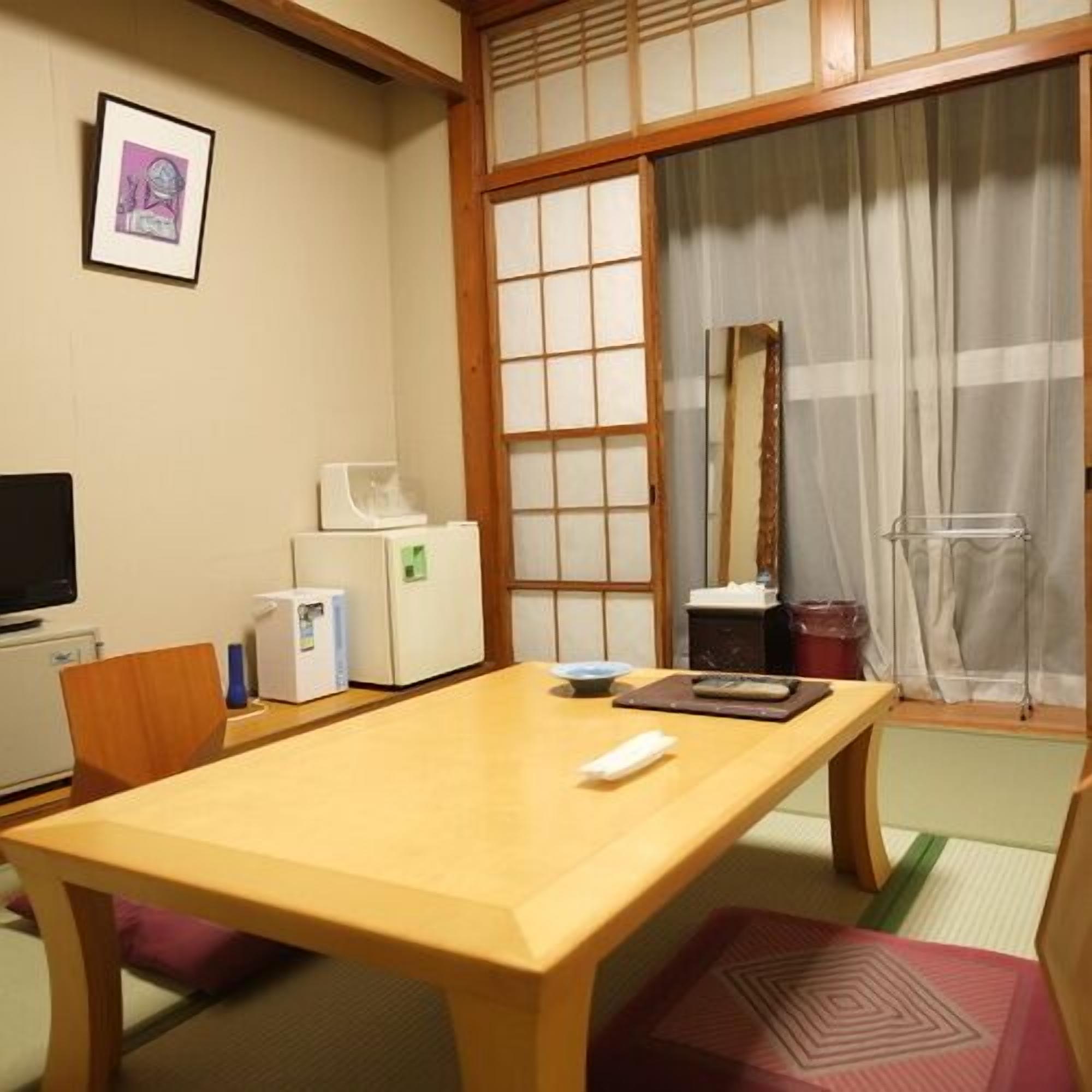 A traditional Japanese room with tatami flooring, a wooden table, a television, and a sliding door.