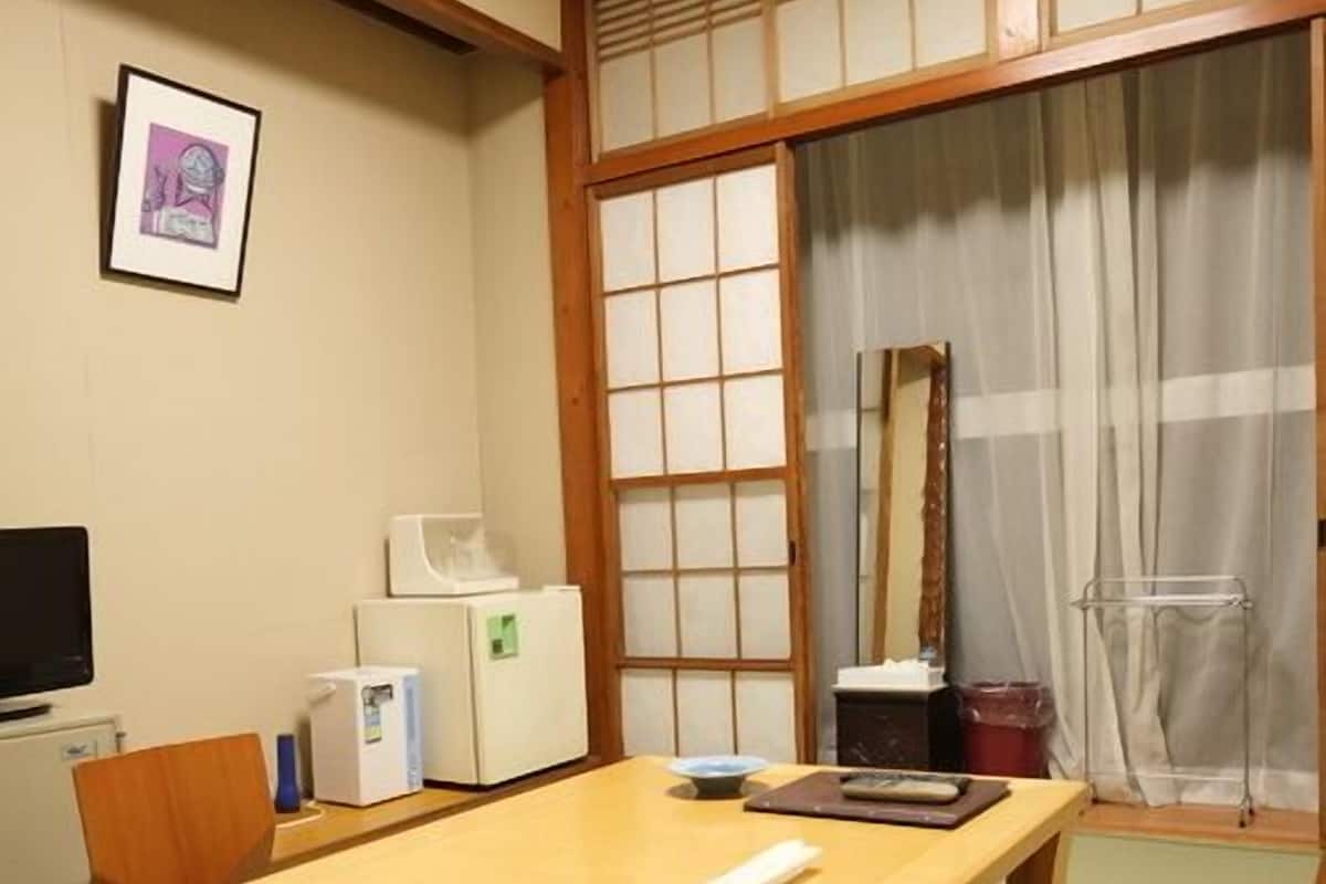 A traditional Japanese room with tatami flooring, a wooden table, a television, and a sliding door.