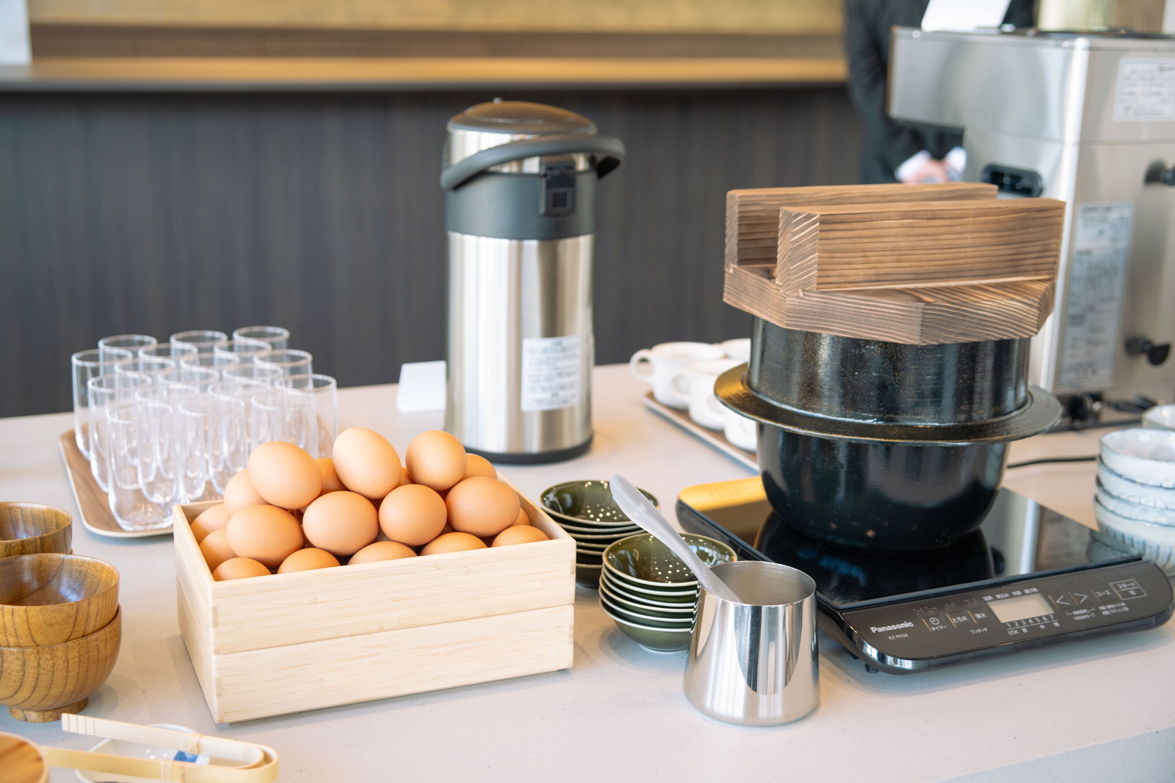 A kitchen counter with a coffee maker, a scale, a wooden egg crate, and several bowls and cups.