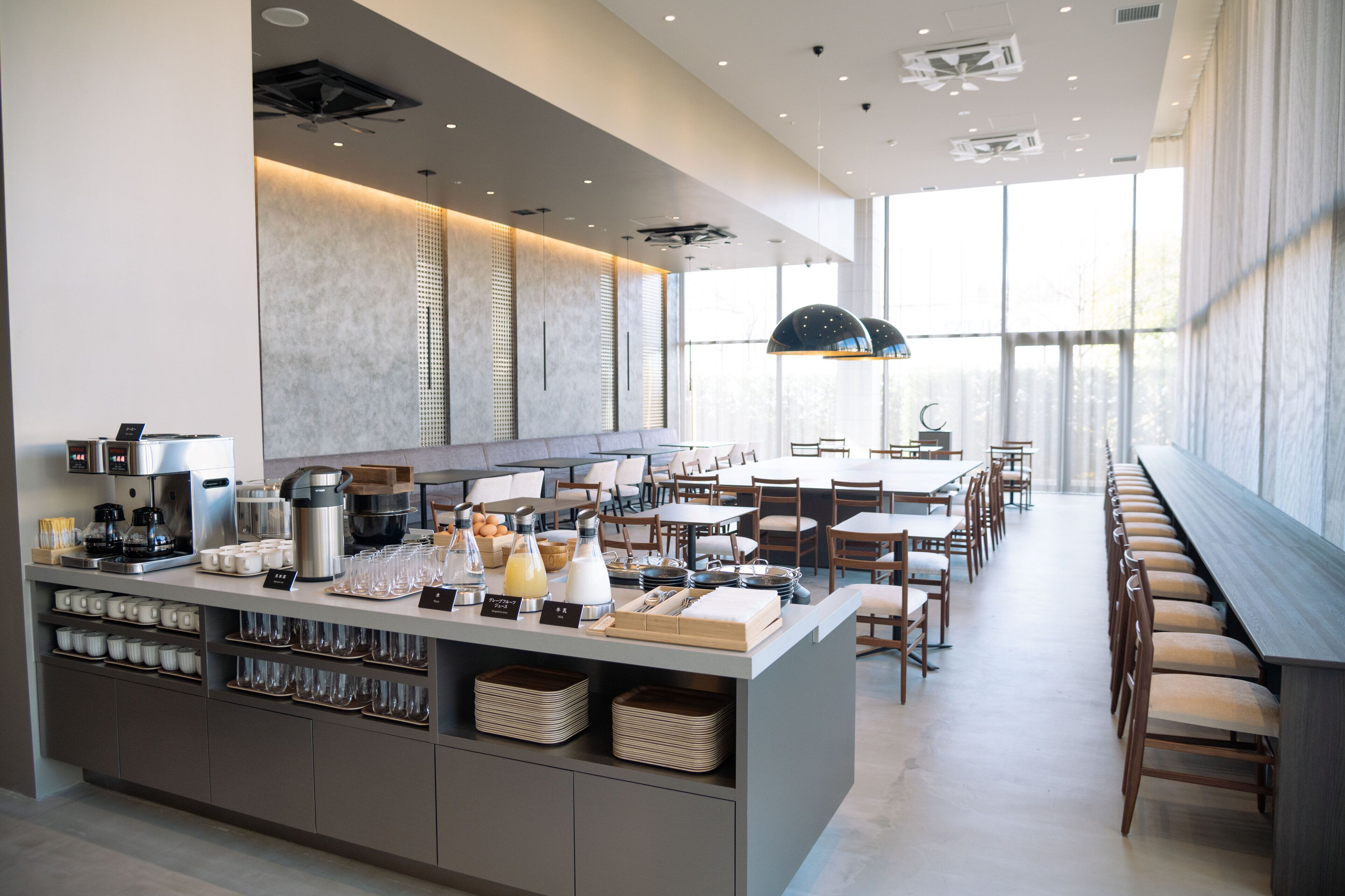 A modern cafe with a long counter, seating area, and large windows.