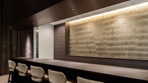 Una zona de bar con una barra alargada, varios taburetes y una pared texturizada detrás de la barra.