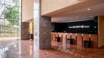 A modern hotel lobby with a reception desk, marble flooring, and large windows offering a view of the outdoors.
