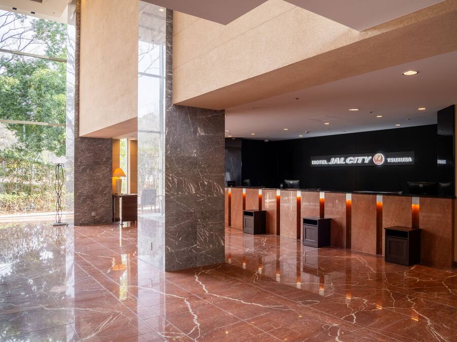 A modern hotel lobby with a reception desk, marble flooring, and large windows offering a view of the outdoors.