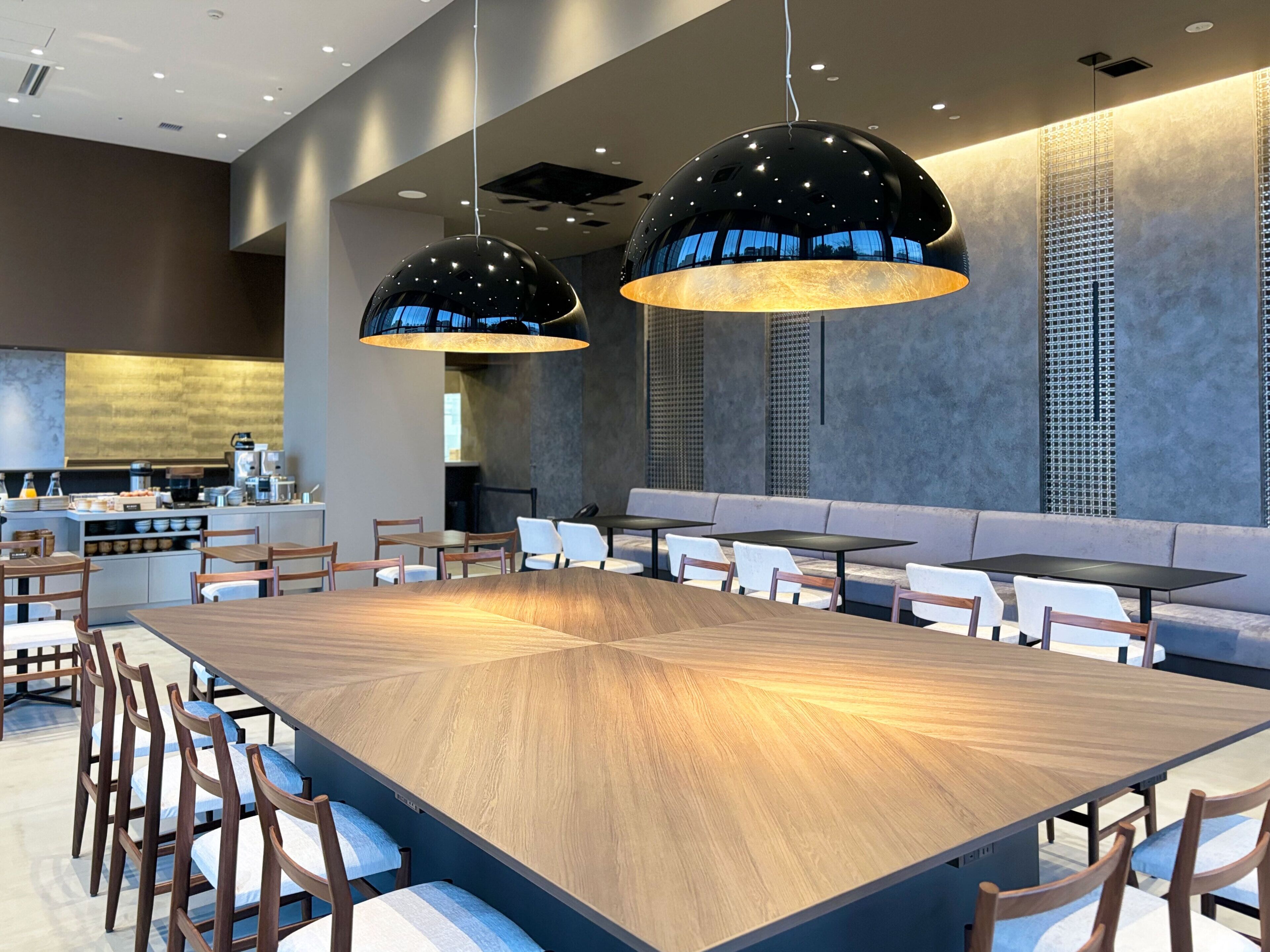 A modern dining area with a long wooden table, multiple chairs, and two large pendant lights.