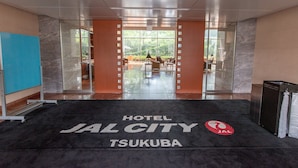 Entrada de un hotel con una alfombra negra que muestra el texto "HOTEL JAL CITY TSUKUBA" y un logotipo rojo.