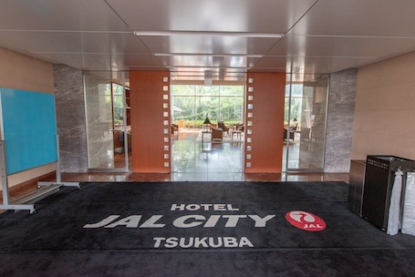A hotel entrance with a black carpet displaying "HOTEL JAL CITY TSUKUBA" and a red logo.