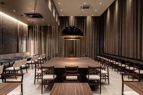 A conference room with a large wooden table, multiple chairs, and a central hanging light fixture.