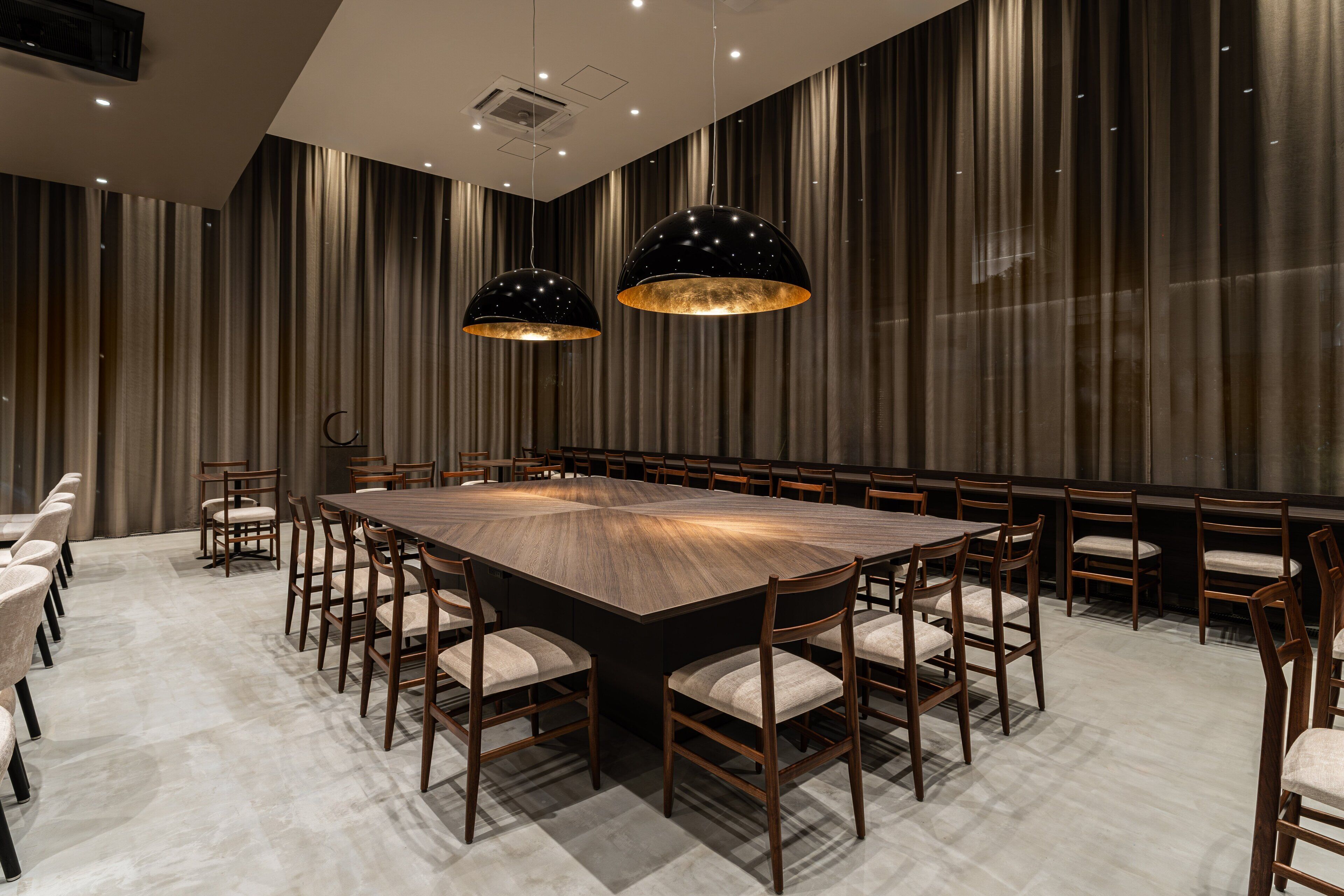 A conference room with a large rectangular table surrounded by chairs, two pendant lights, and a striped curtain wall.