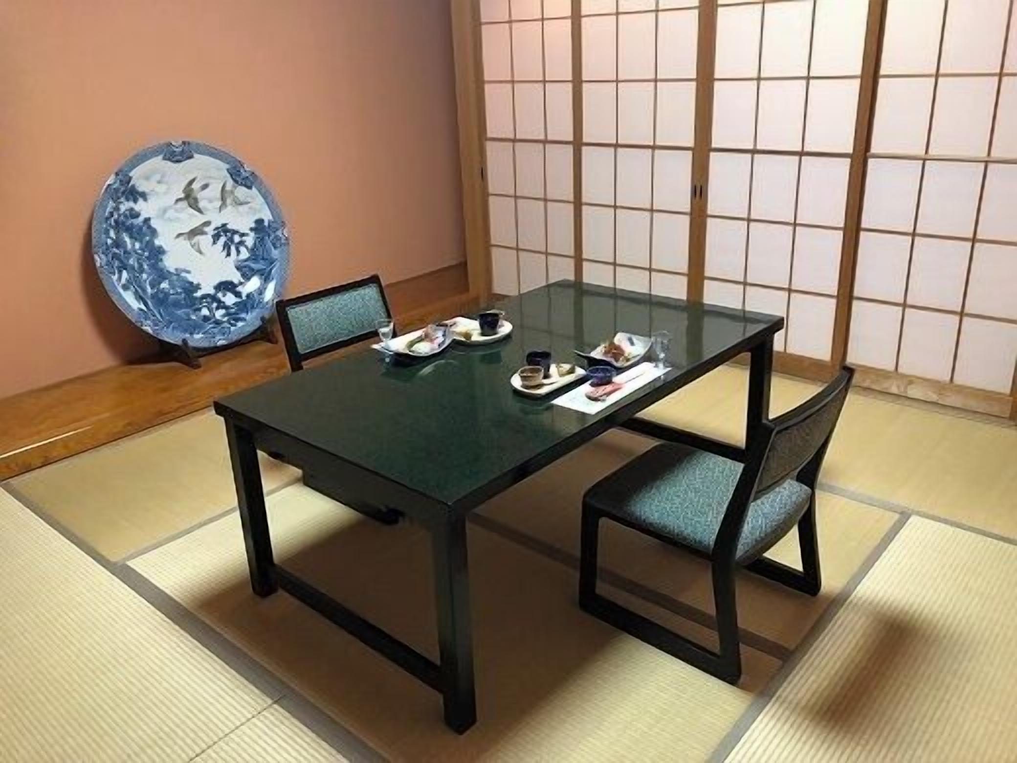 A traditional Japanese-style room with tatami flooring, a low table with a dark tabletop, and two chairs with cushions.