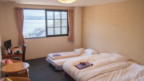 Une chambre d’hôtel avec deux lits simples, un bureau avec un ordinateur, une chaise et une vue sur une étendue d’eau par la fenêtre.