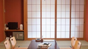 Une pièce de style japonais traditionnel, avec un sol recouvert de tatamis, une table basse avec des coussins, un téléviseur et des portes coulissantes en papier de riz (shoji).