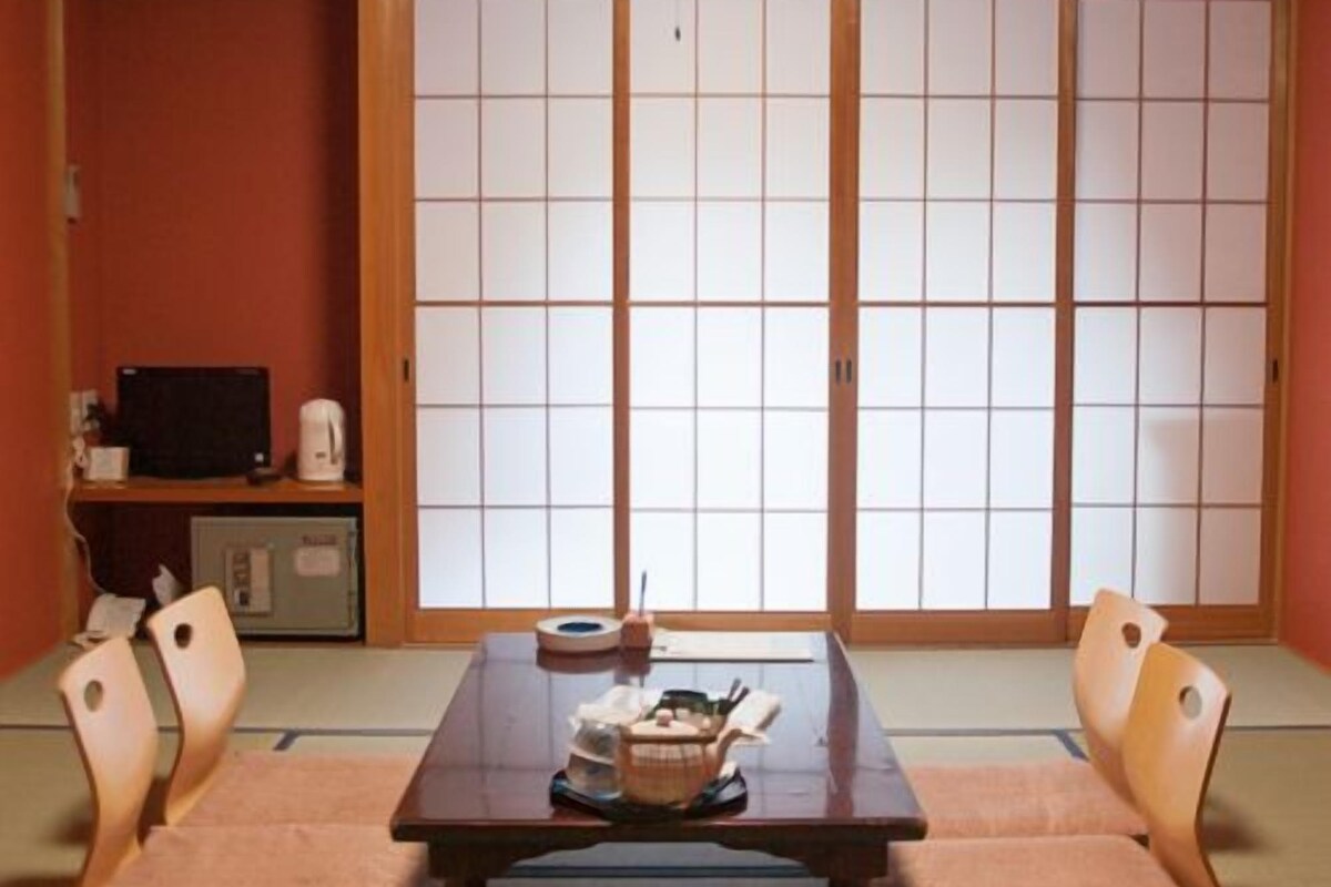 A traditional Japanese room with tatami flooring, a low table with cushions, a television, and sliding shoji doors.