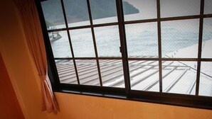 Une pièce dotée d’une grande fenêtre donnant sur un quai et l’eau. On y trouve deux fauteuils en osier et une petite table ronde.