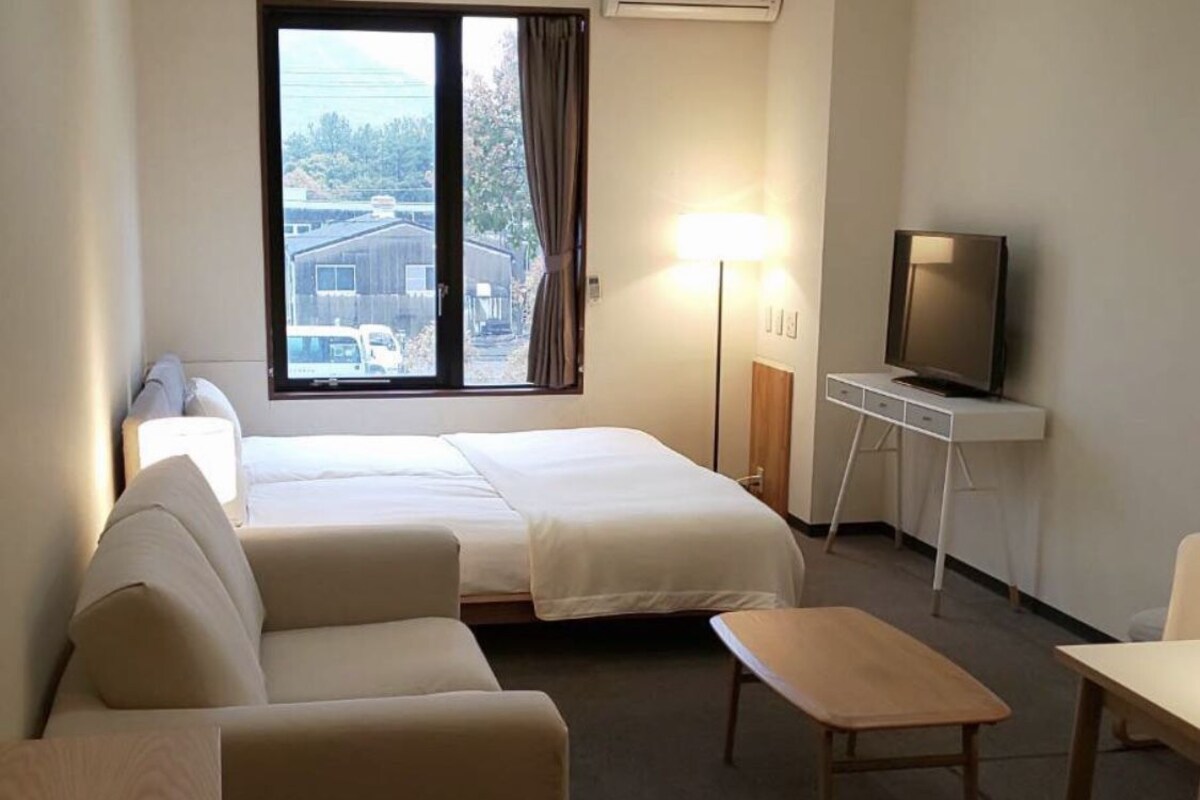 A hotel room with a bed, a sofa, a small table, a TV, and a lamp.