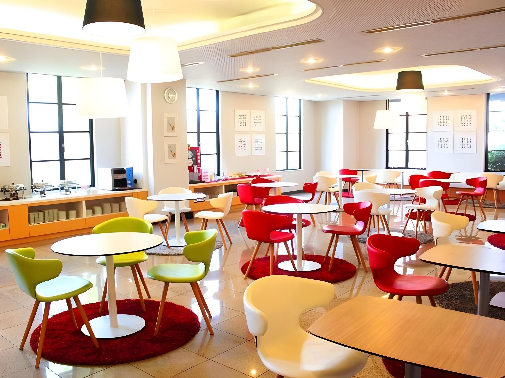Een modern café met ronde tafels en kleurrijke stoelen, grote ramen en een schoon, licht interieur.
