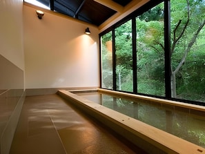 A spa area with a wooden bench, a glass enclosure, and a view of a forest through large windows. - Sakaide Plaza Hotel (Sakaide)