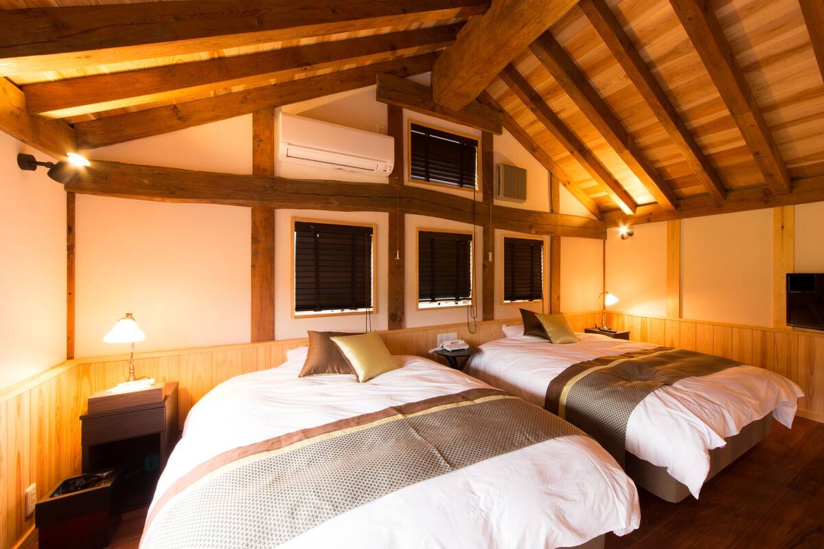 A room with two beds, wooden beams, an air conditioning unit, a television, and a lamp.