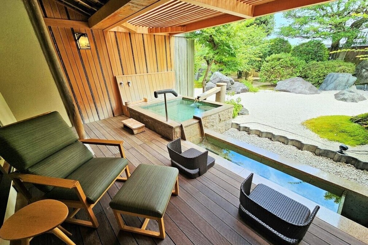 A wooden deck with lounge chairs and a hot tub overlooking a garden with rocks and greenery.