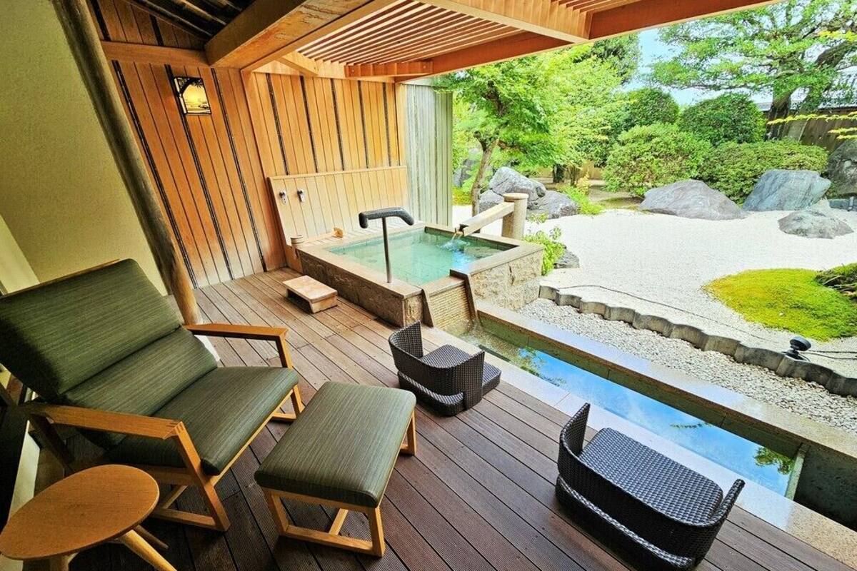 A wooden deck with lounge chairs and a hot tub overlooking a garden with rocks and greenery.