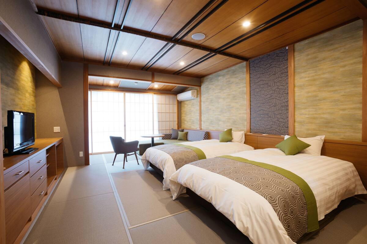 A hotel room with two beds, a desk, a chair, and a television.