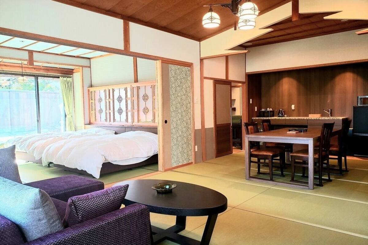 A room with a bed, a dining table with chairs, a sofa, and a kitchen area.