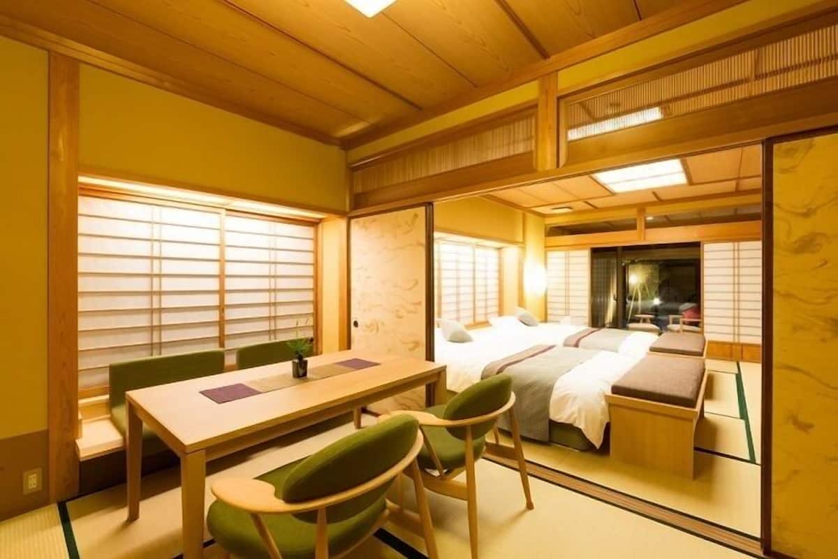 A traditional Japanese-style room with tatami flooring, a low table with chairs, a bed with futon beds, and sliding doors.